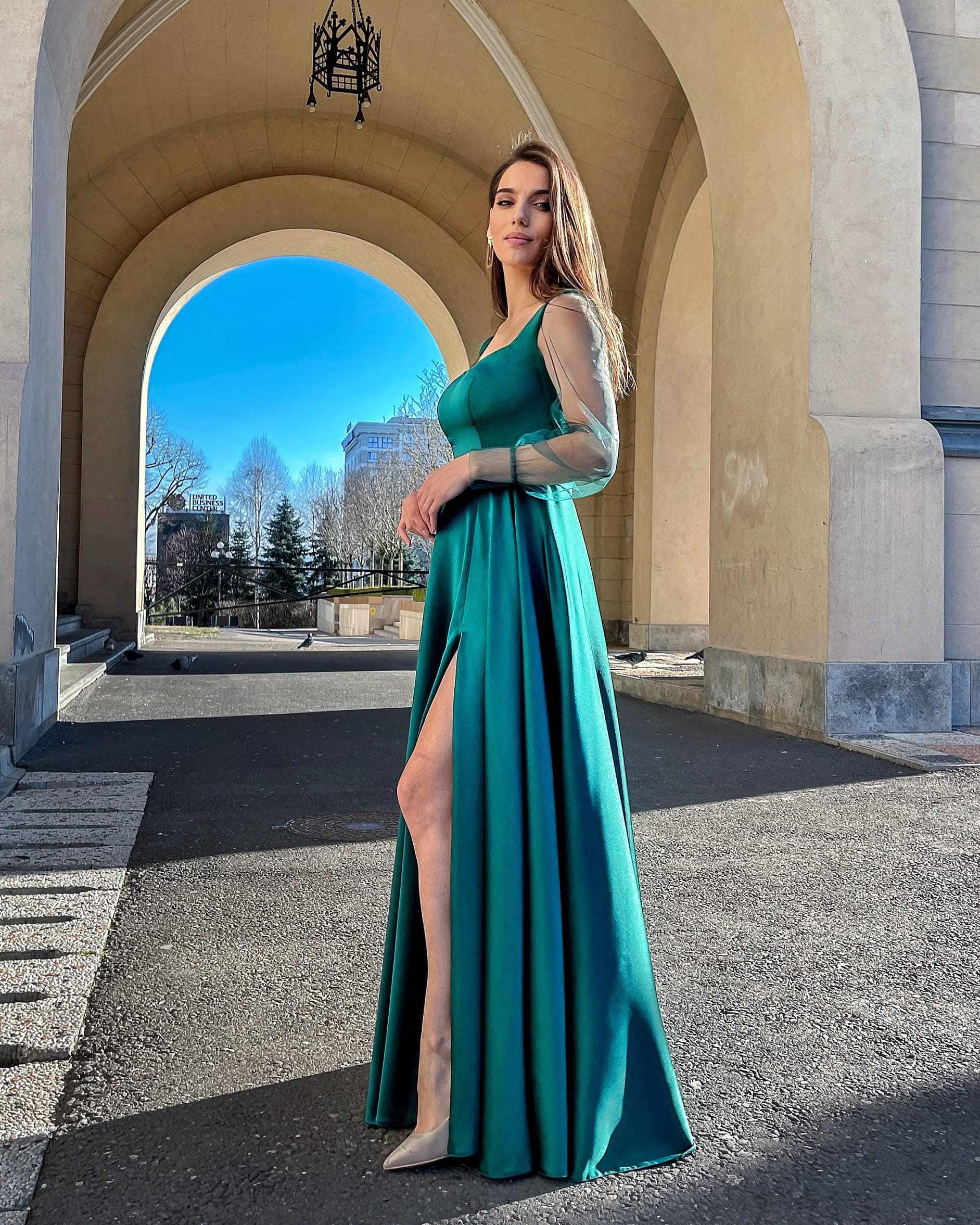 Rochie lunga verde smarald din satin cu mâneci transparente și șlit lateral.