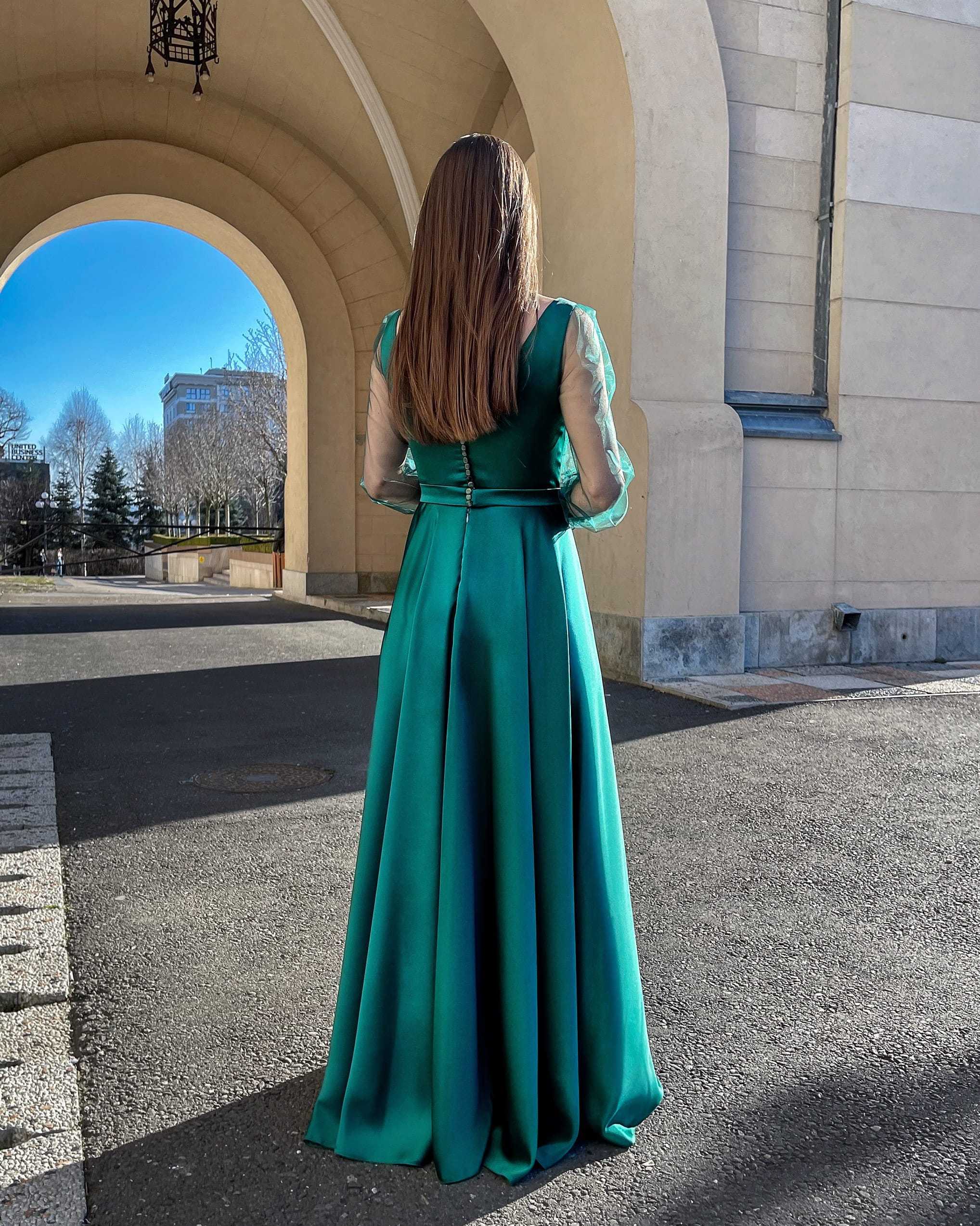 Rochie lunga verde smarald din satin cu mâneci transparente și spate cu nasturi, eleganță sofisticată pentru evenimente speciale.