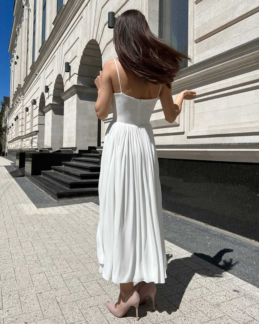 Rochie alba elegantă cu bretele și slit, accesorizată cu centură, vedere din spate.