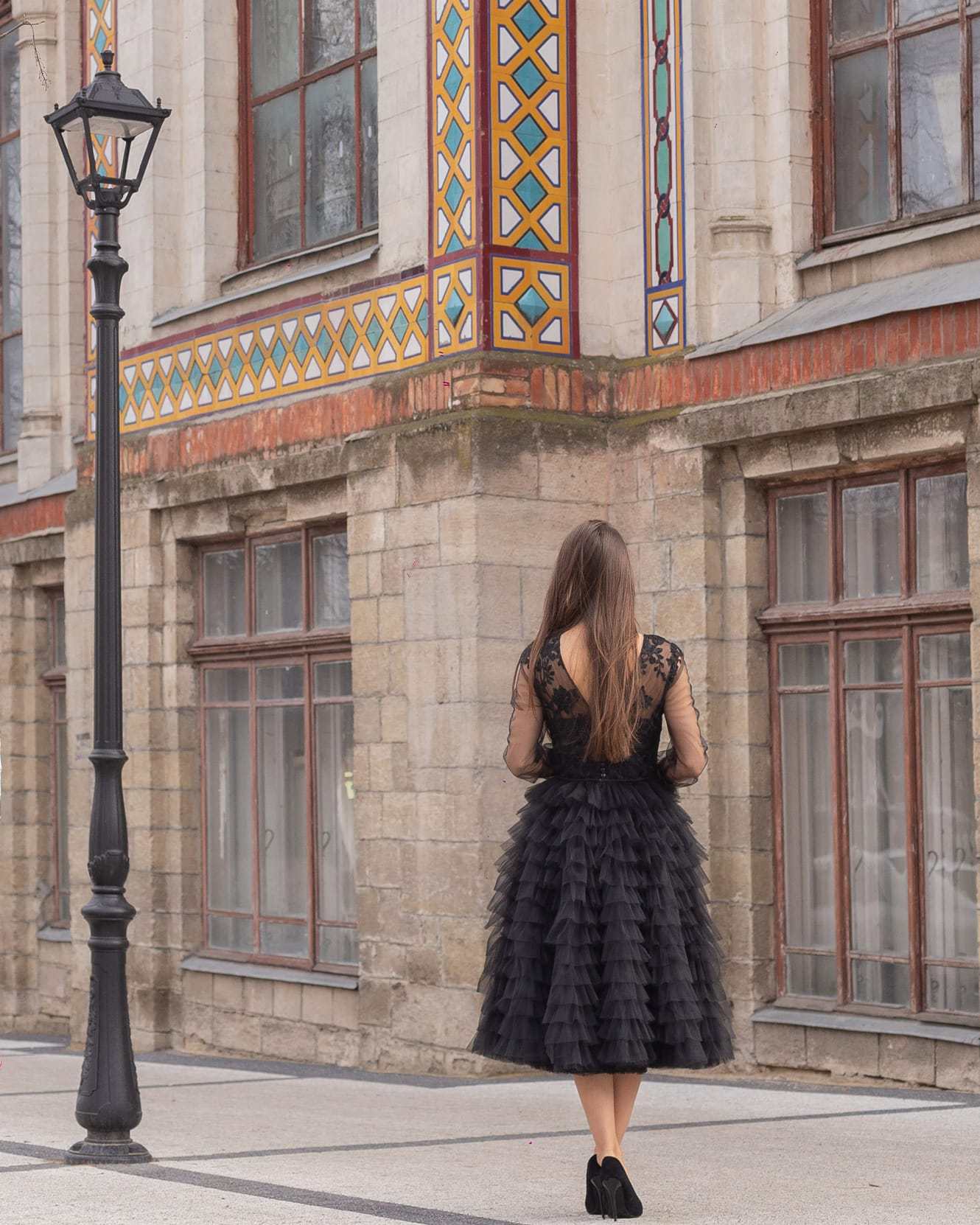 Rochie neagră de ocazie din dantelă cu mâneci lungi transparente, lungime midi, fundal urban.